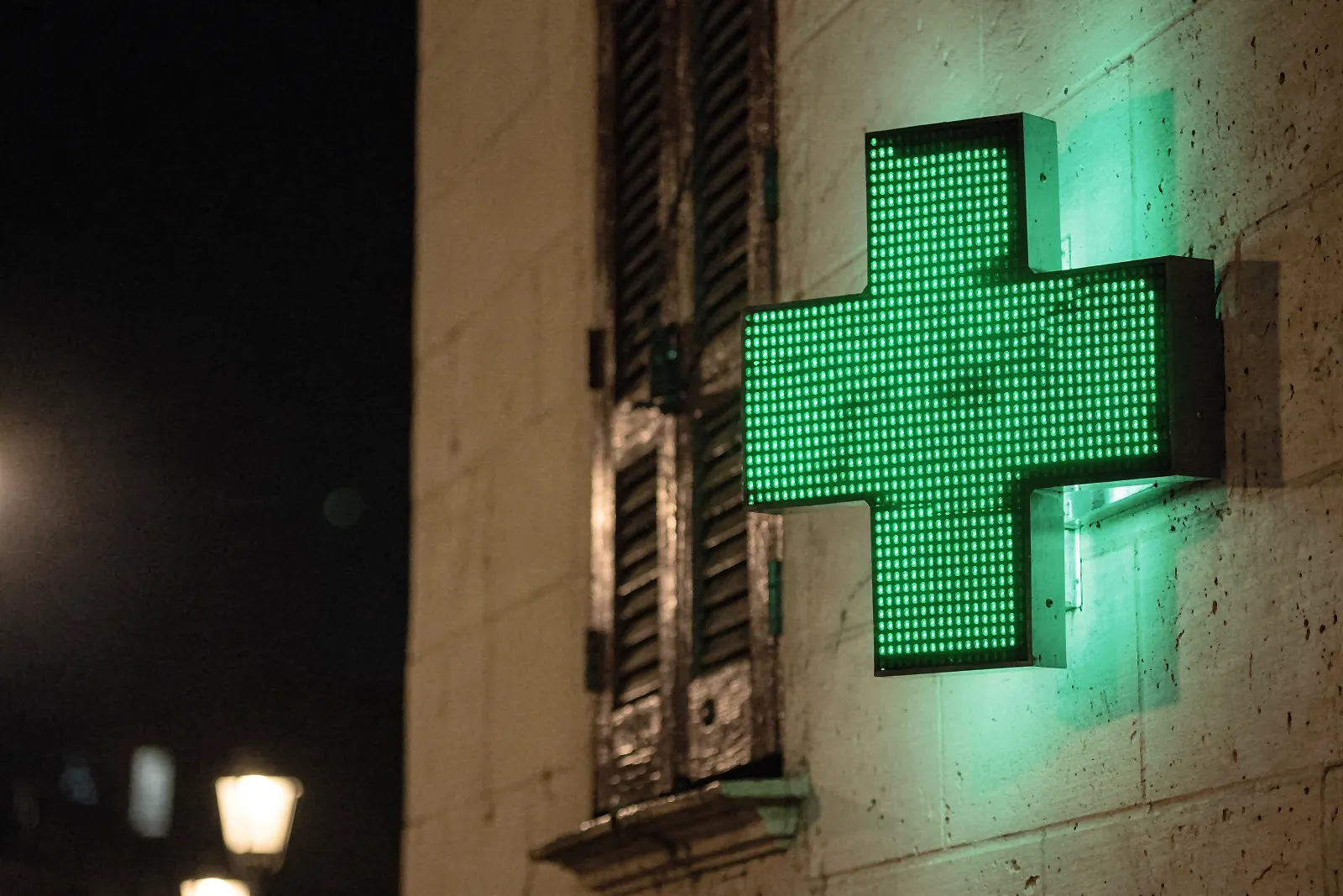 Illuminated green pharmacy cross on a building at night (illustrative image)