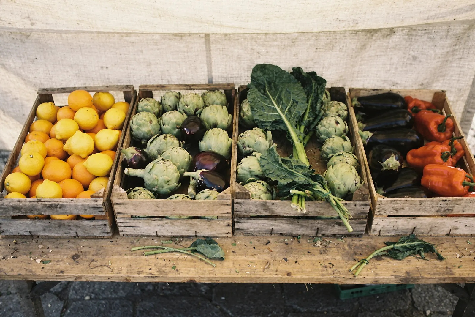 Cajas de madera con limones, naranjas, alcachofas, berenjenas, acelgas y pimientos en un puesto de mercado (imagen ilustrativa)